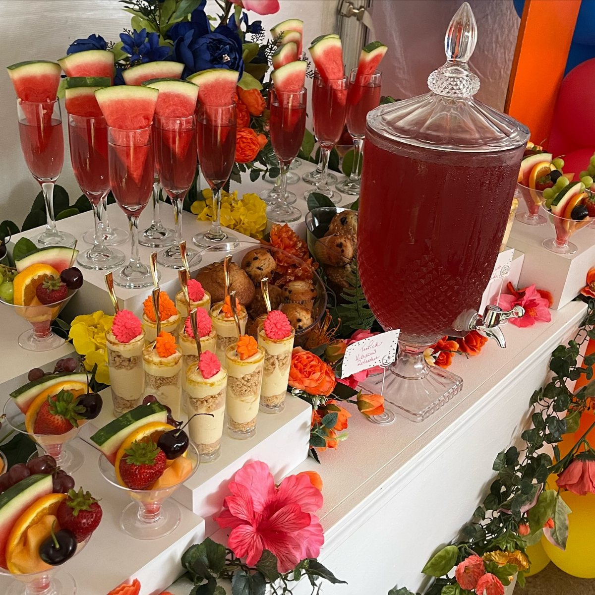 A festive table display with red fruit drinks, dessert cups, and colorful fruit bowls.