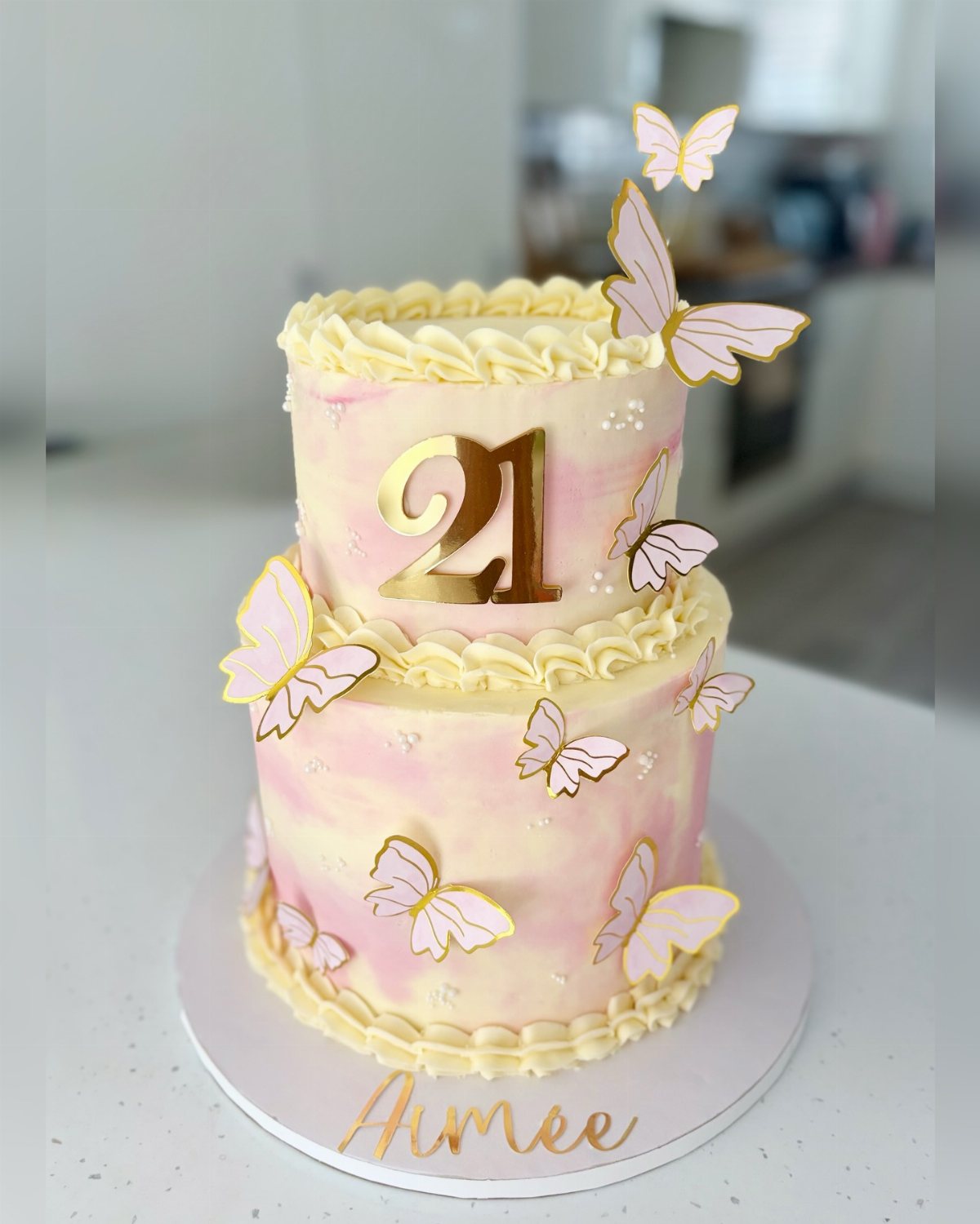 Two-tiered cake with gold butterflies and a '21' decoration.