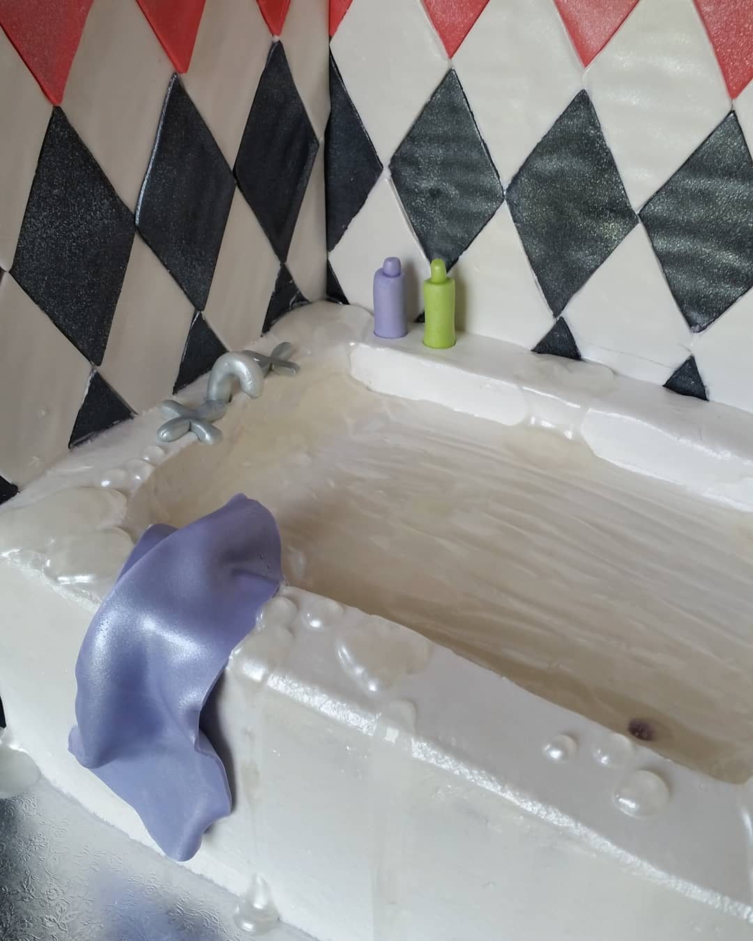 A hyper-realistic white bathtub cake with purple fondant cloth and diamond patterned background.