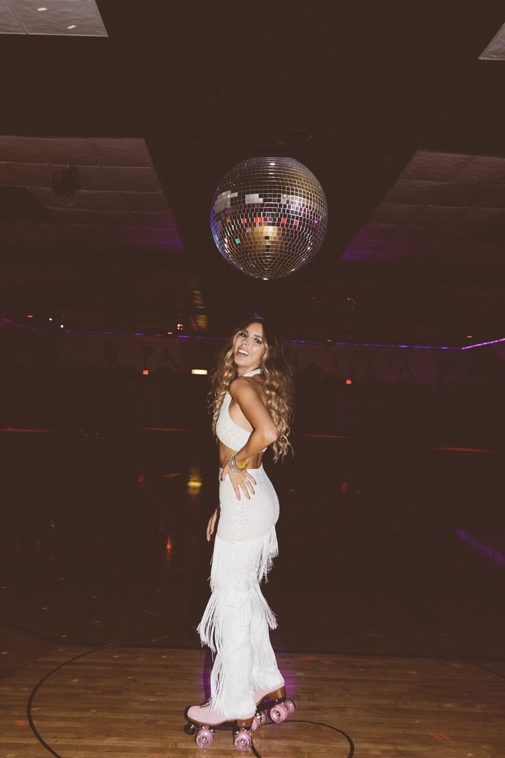 A woman in white fringe clothing posing on roller skates under a disco ball.