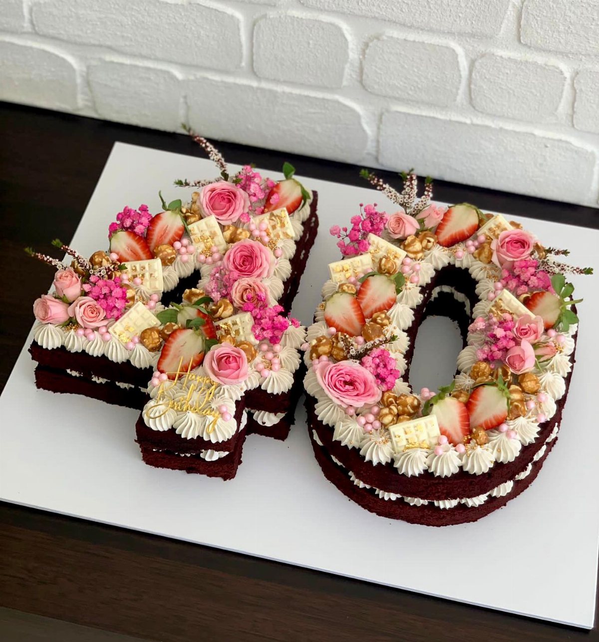 Red velvet cake shaped like the number 40 decorated with pink roses and strawberries.