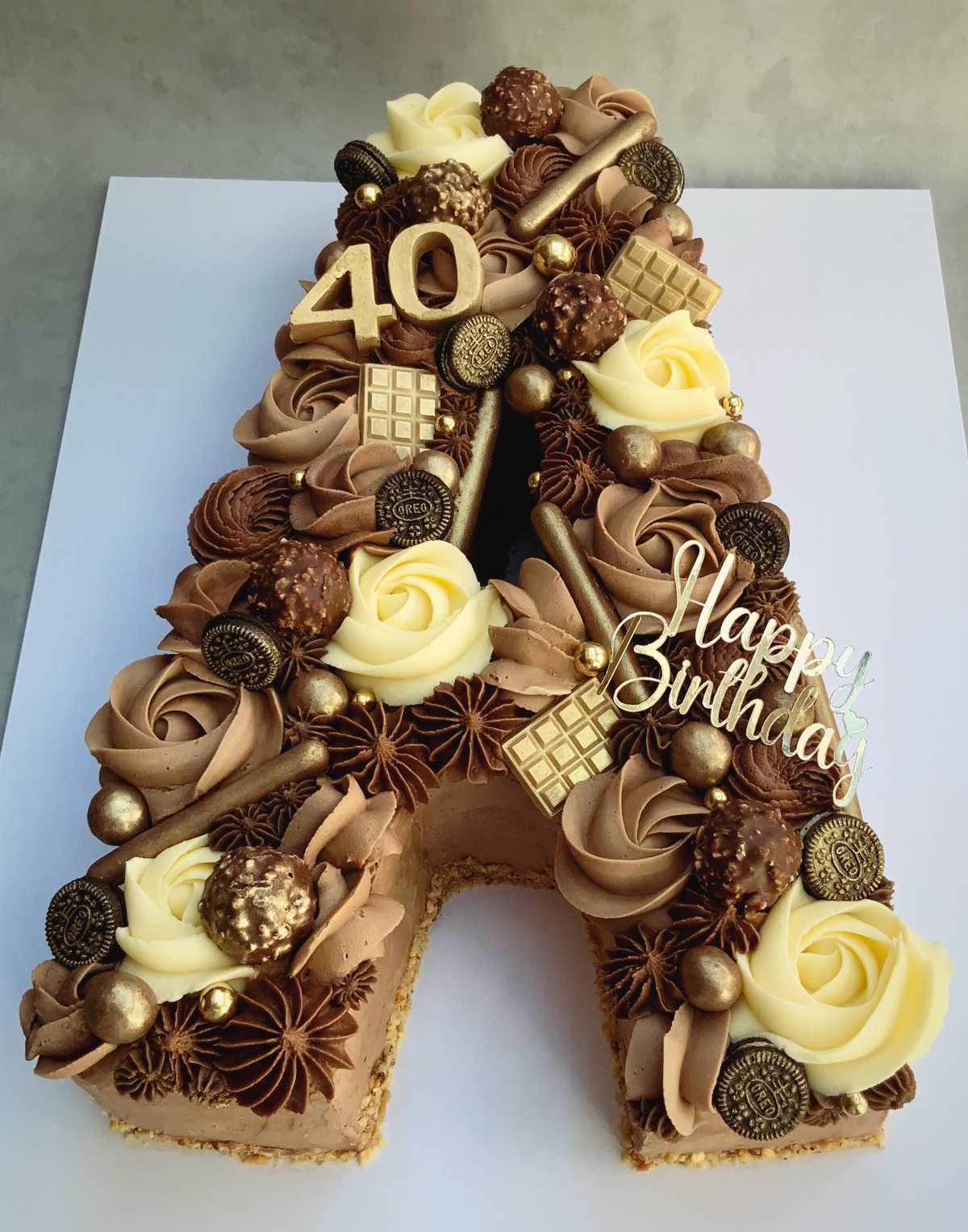 Letter A shaped cake decorated with chocolate rosettes, truffles, and gold birthday toppers.