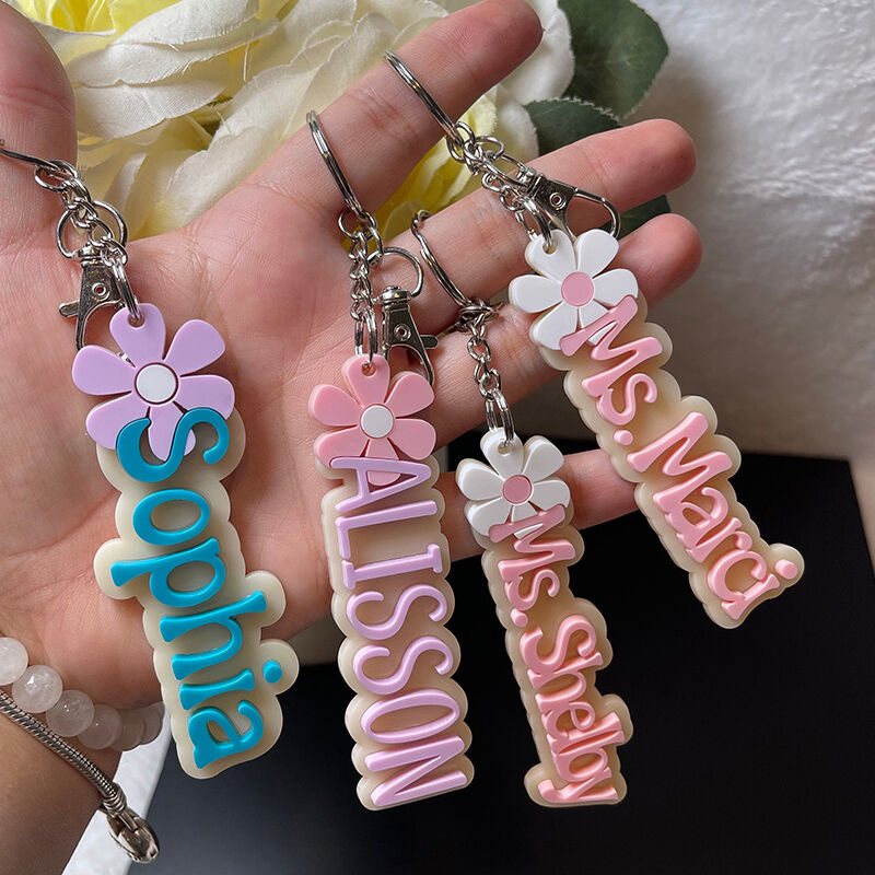 A hand holding four colorful customized name keychains with flower decorations.