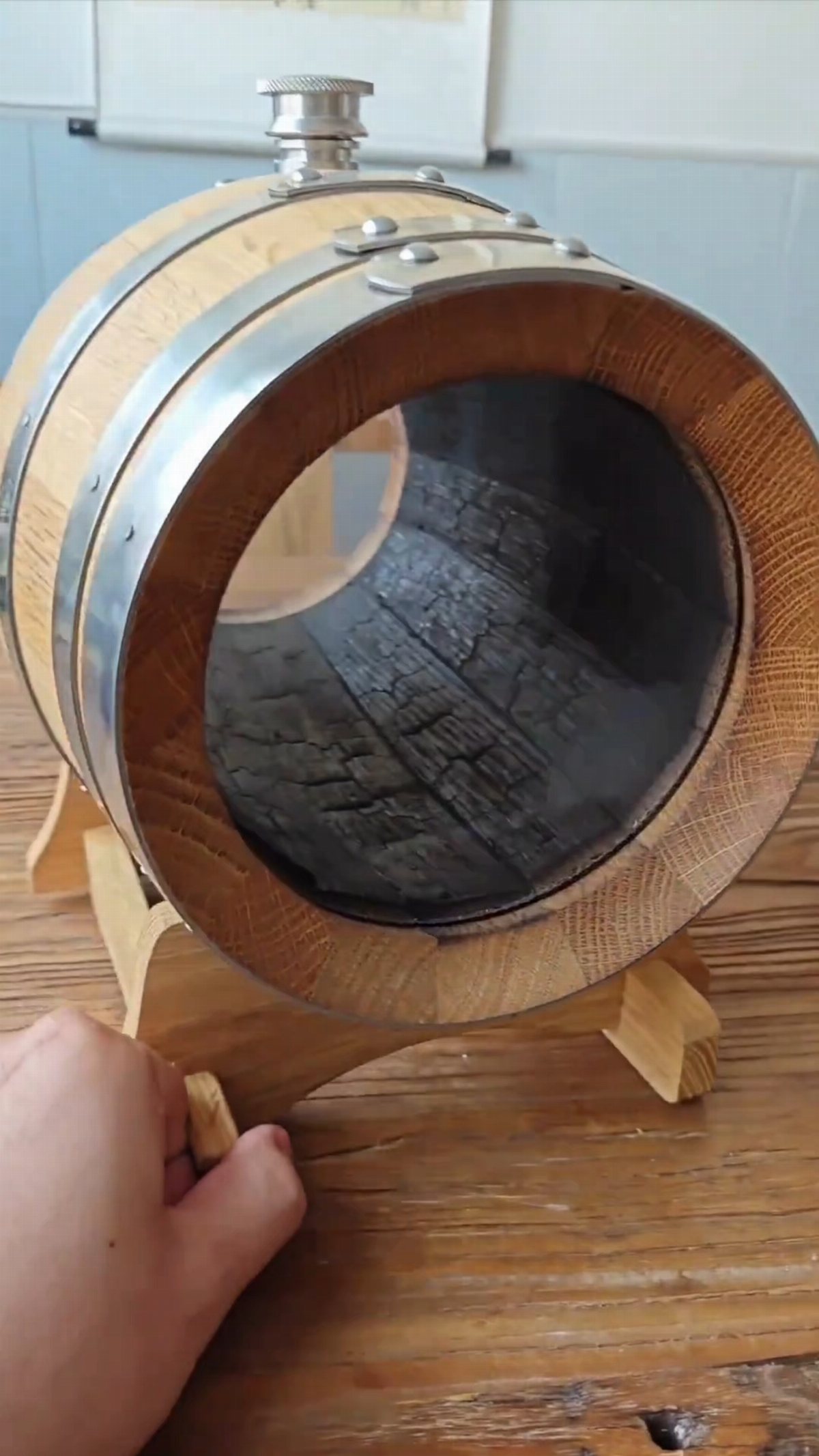 A small wooden whiskey barrel with a glass viewing window sitting on a wooden stand.