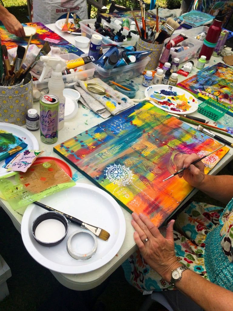 A person painting on a colorful canvas at an art table.