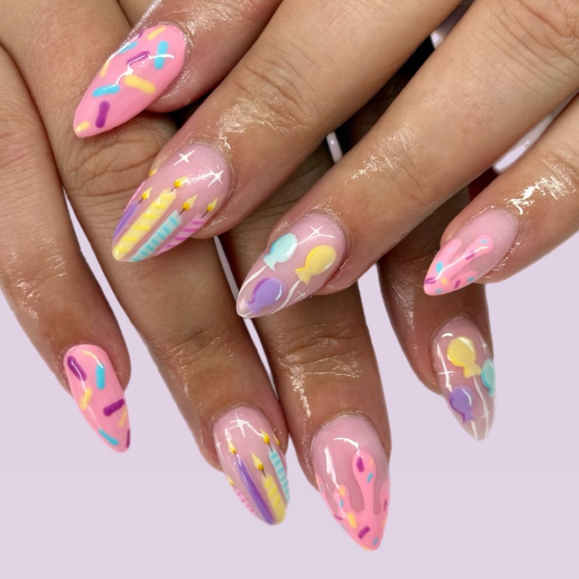 Long almond-shaped pink nails decorated with colorful pastel birthday candles and sprinkles.