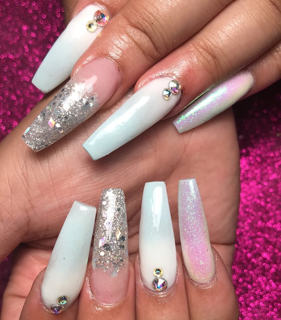 Long coffin-shaped nails with light blue, pink ombre, and silver glitter accents on a pink background.