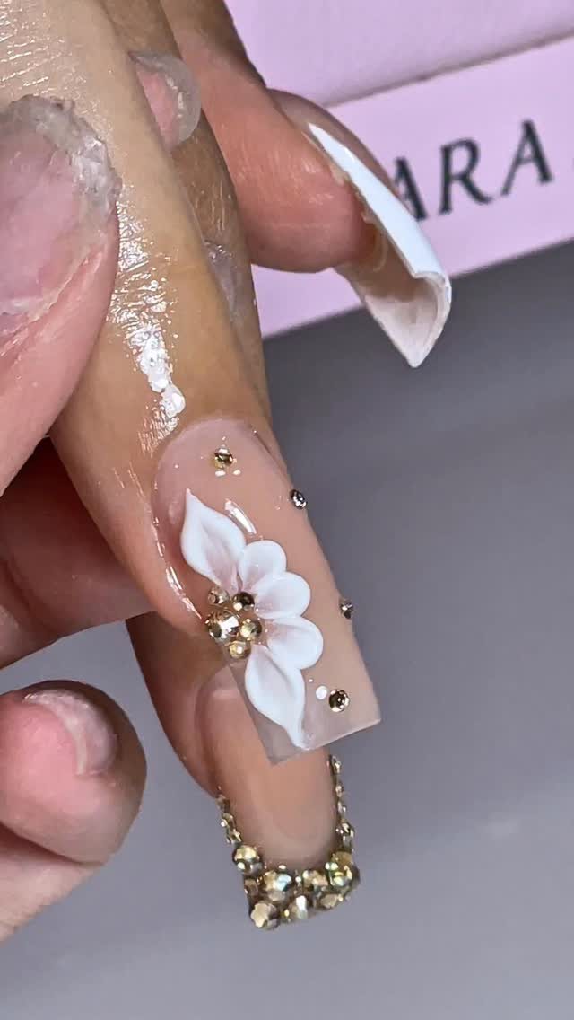 Long clear acrylic nail with a white 3D flower and gold rhinestone embellishments.
