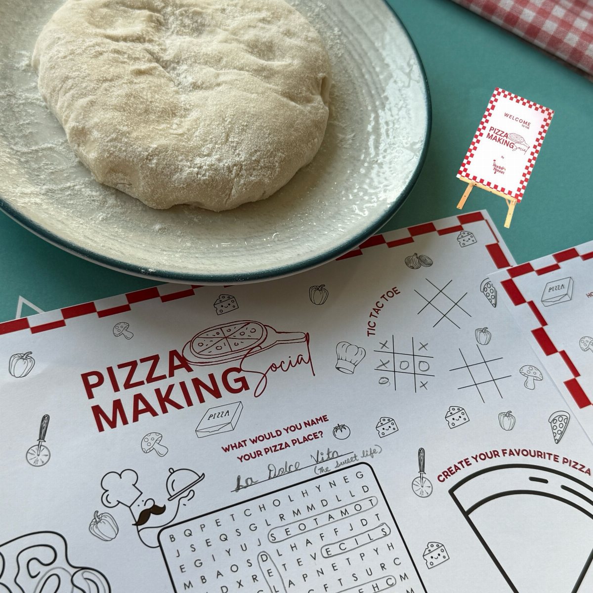 Pizza dough on a plate next to a themed pizza making activity placemat.