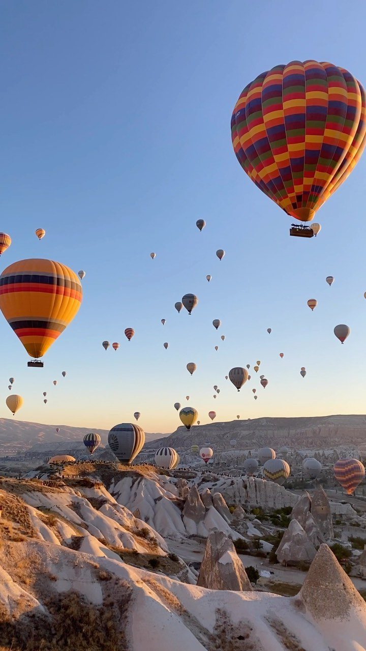 Colorful hot air balloons floating over a vast, rocky canyon landscape under a clear sky.