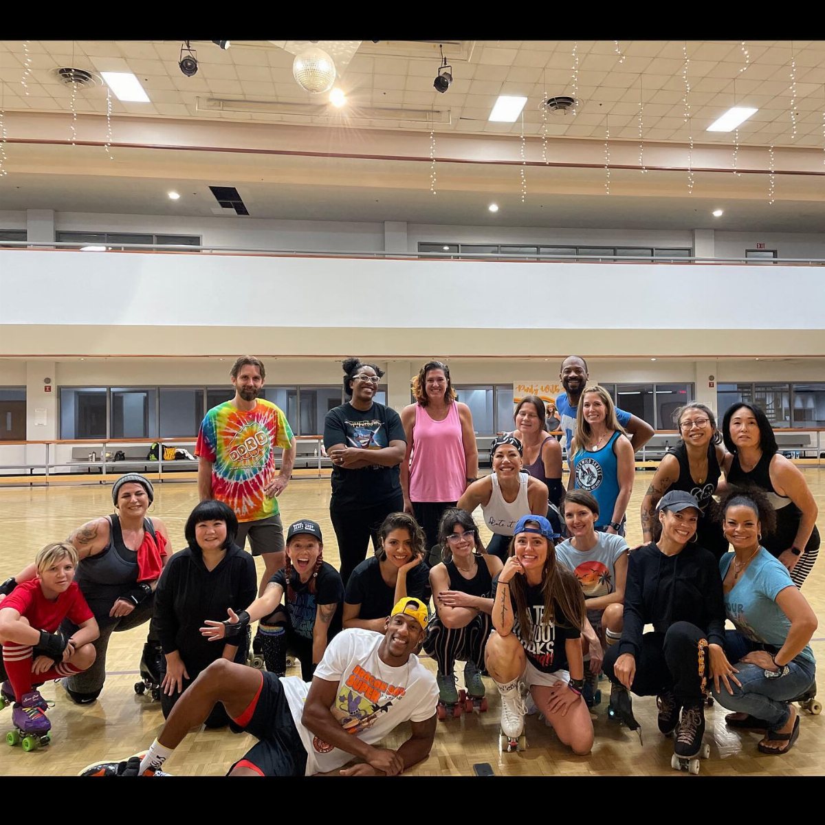 A diverse group of people posing together on a wooden roller skating rink.