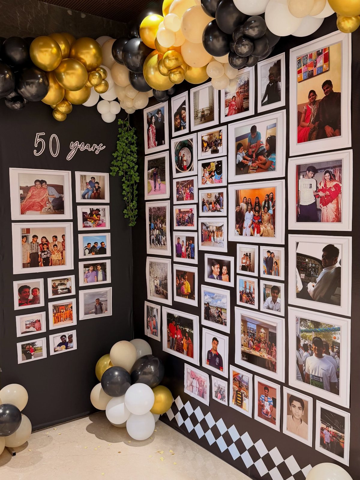A wall covered in framed photographs with gold and black balloons for a 50th birthday.