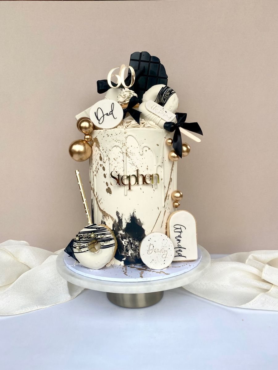 A white and black decorated cake with gold accents, featuring a sixty topper and nameplate.