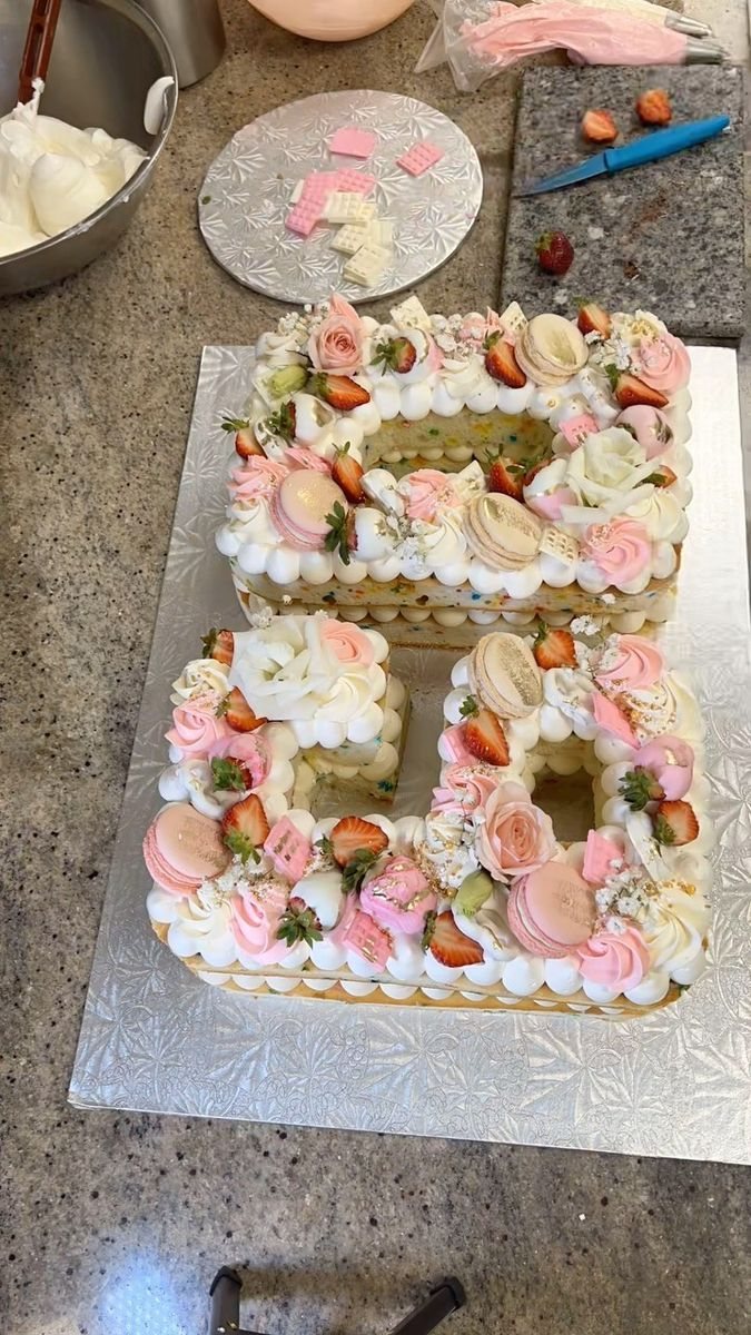 Letter-shaped cakes decorated with pink frosting, strawberries, macarons, and delicate flowers on a silver tray.