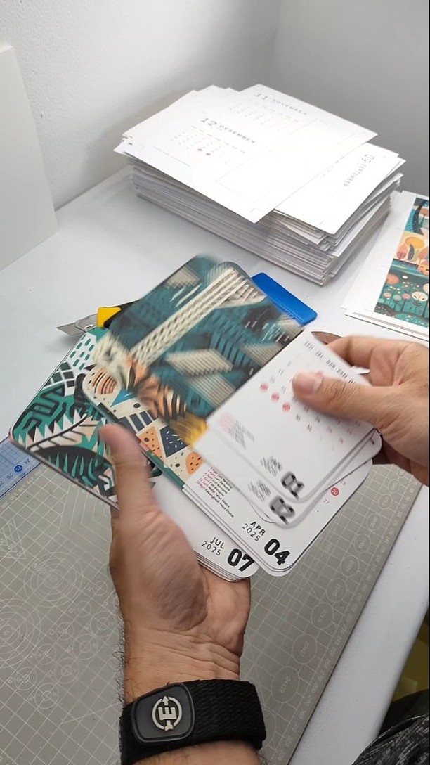 Hands holding a stack of colorful customized calendars with tropical patterns and printed dates.