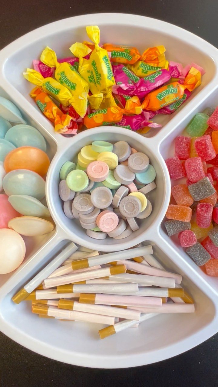 A white divided tray filled with various colorful wrapped candies, gummy sweets, and pastel discs.