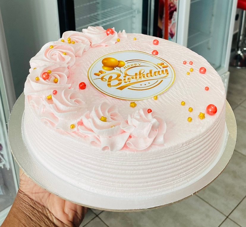 A single-tier pink buttercream cake decorated with swirls, gold pearls, and a Happy Birthday topper.