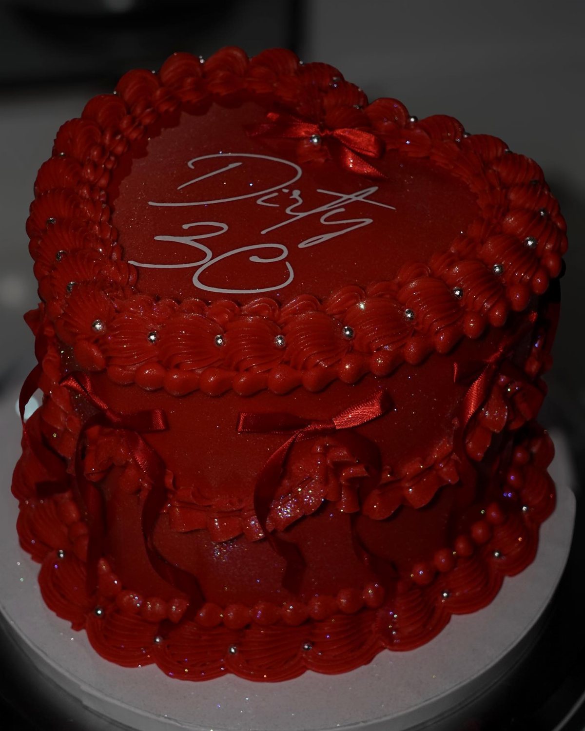 Red heart-shaped cake with white 'Dirty 30' icing and silver pearl decorations.