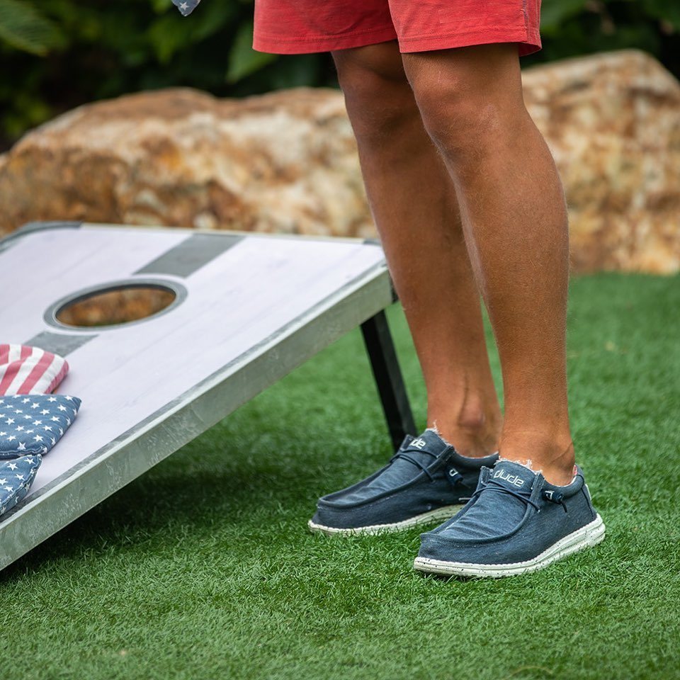 A person standing on grass next to a white cornhole game board.