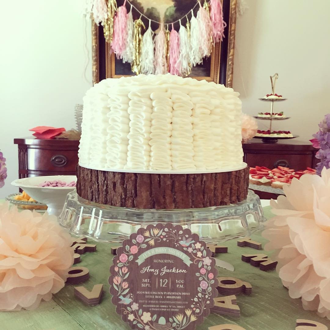 A white frosted cake on a glass stand with a floral invitation in front.