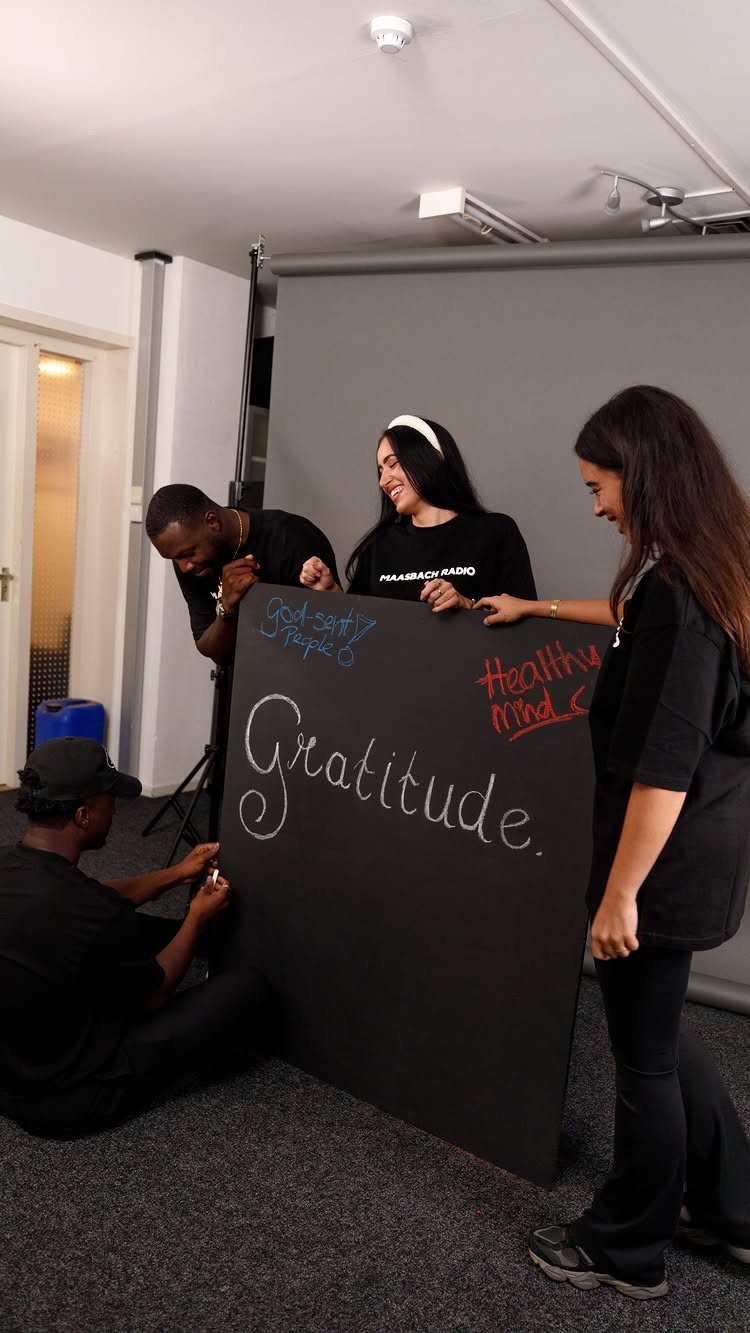 Four people working together to write on a large black gratitude board.