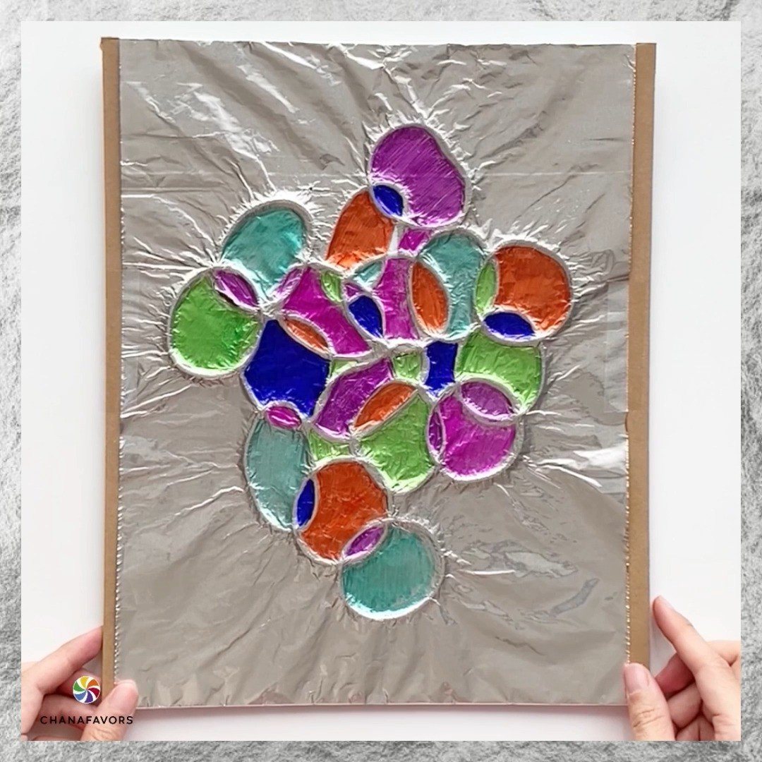 Hands holding a piece of colorful abstract art made with silver foil and translucent shapes.