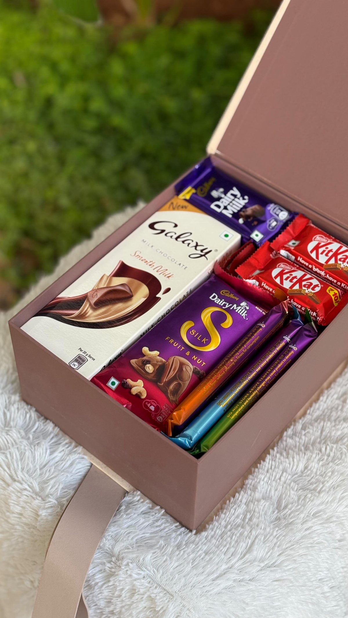 An open mauve gift box filled with various branded chocolate bars on white fluff.