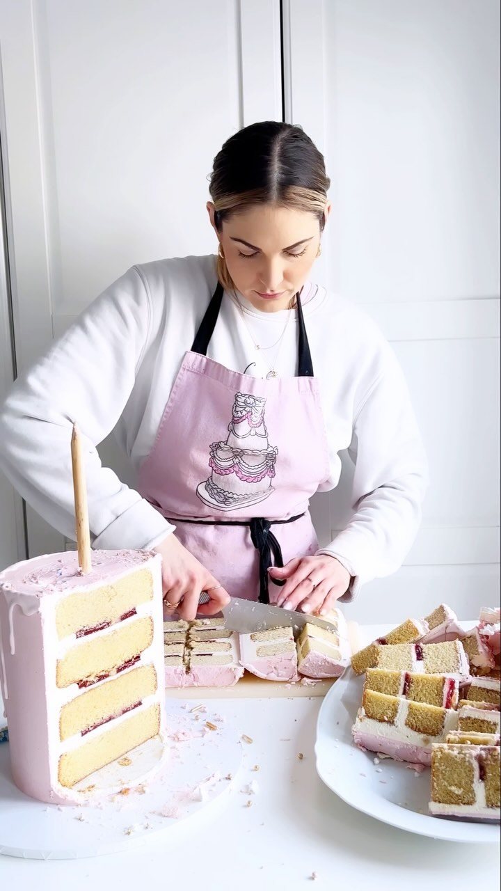 A woman slicing a pink layered cake into individual rectangular servings on a white table.