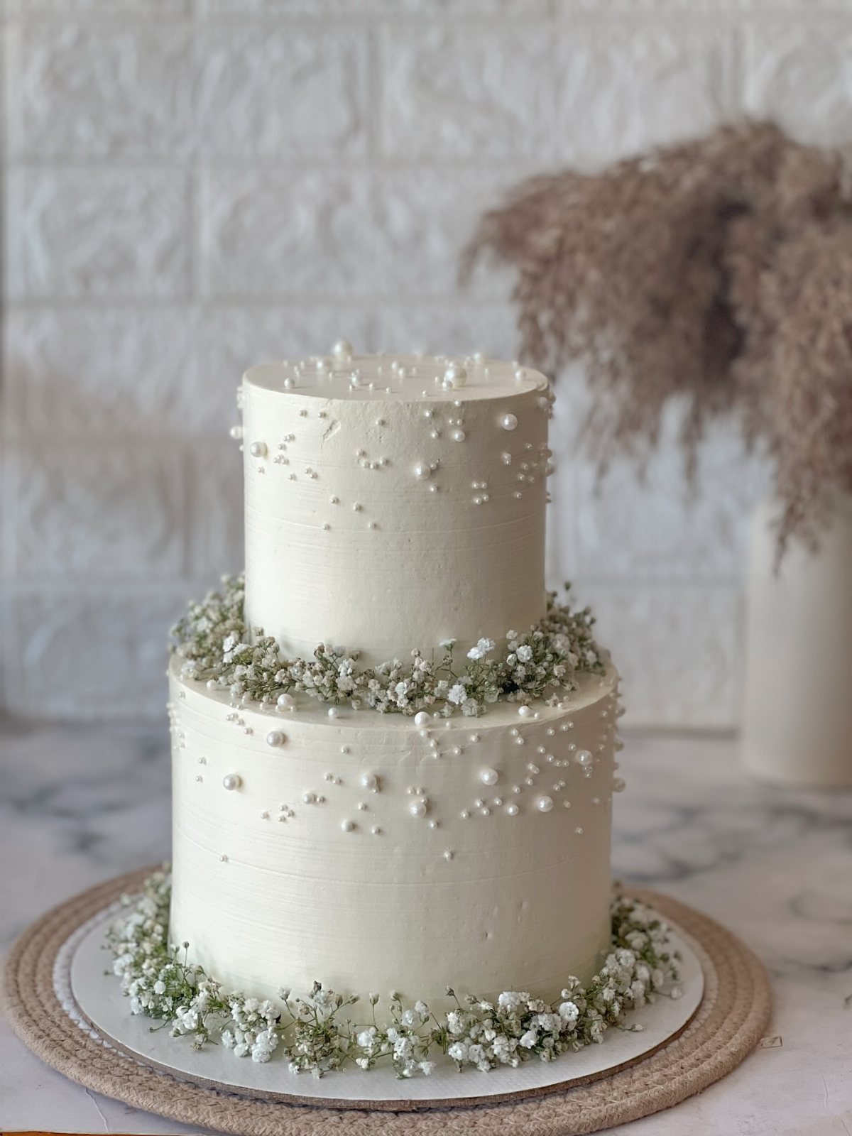 Two-tiered white buttercream wedding cake decorated with small pearls and baby's breath flowers.