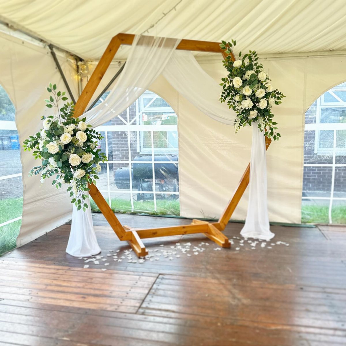 13 Archway for Wedding Ceremony Ideas That Actually Photograph Well 8 Wooden hexagon wedding arch decorated with white roses, greenery, and flowing white fabric inside a tent.