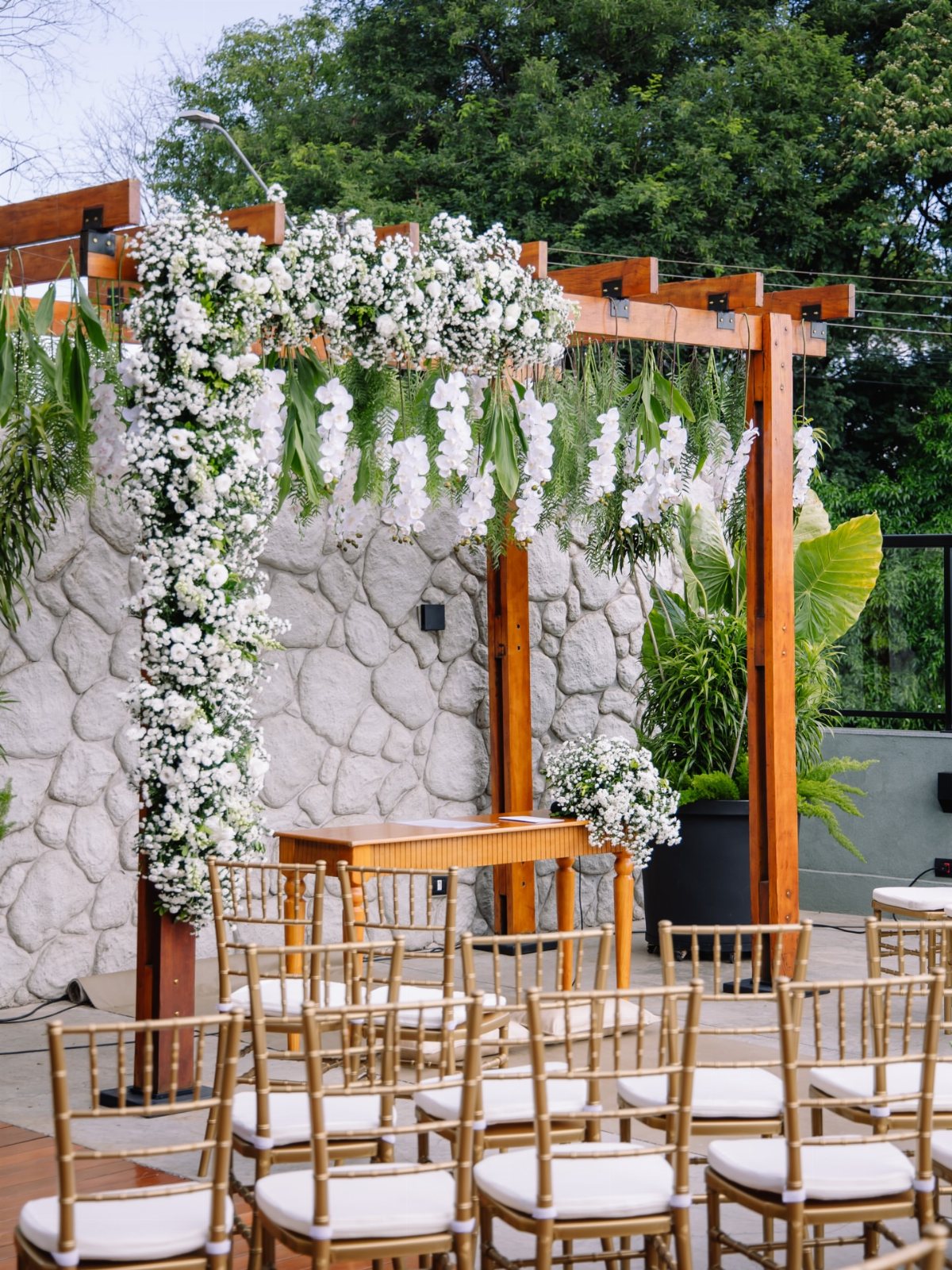13 Archway for Wedding Ceremony Ideas That Actually Photograph Well 11 Wooden pergola decorated with white flowers and greenery overlooking gold wedding chairs.