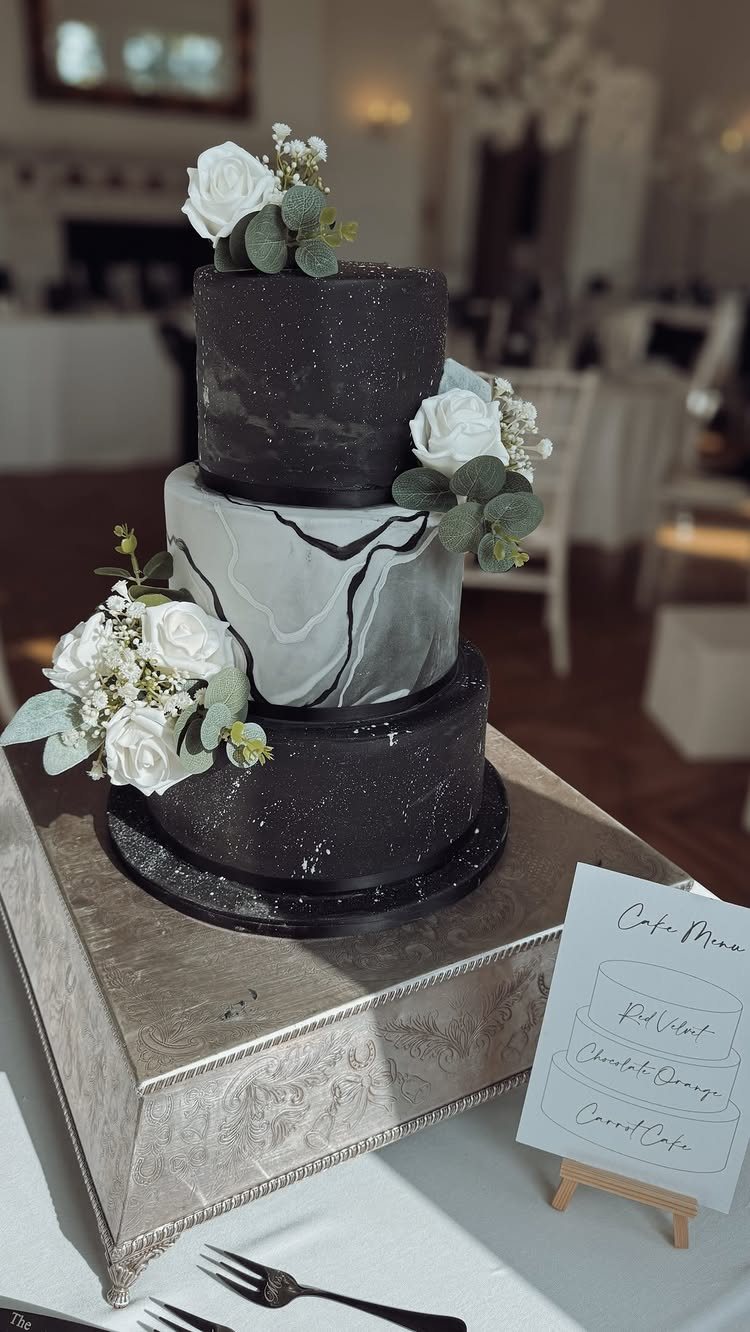 13 Black and White Wedding Decor Ideas for an Elegant Celebration 7 A three-tier black and white wedding cake decorated with white roses and green leaves.