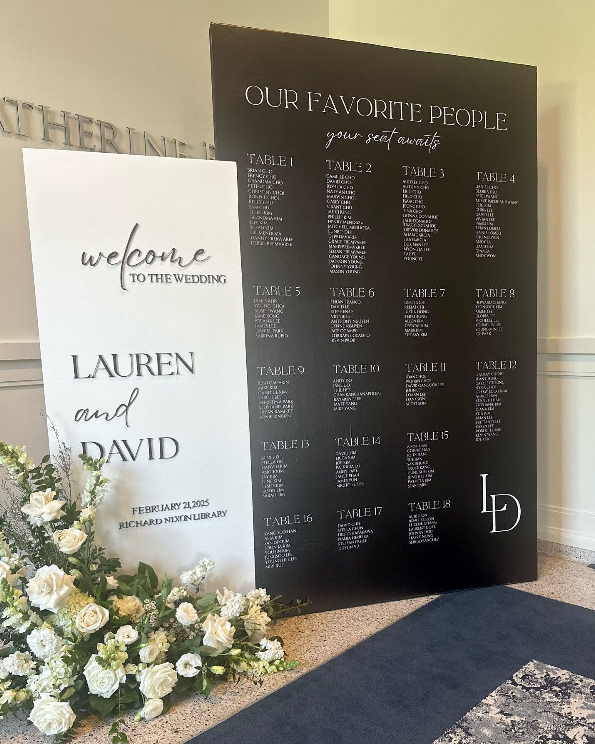 13 Black and White Wedding Decor Ideas for an Elegant Celebration 2 Black and white wedding welcome sign and seating chart with white floral arrangements at the base.