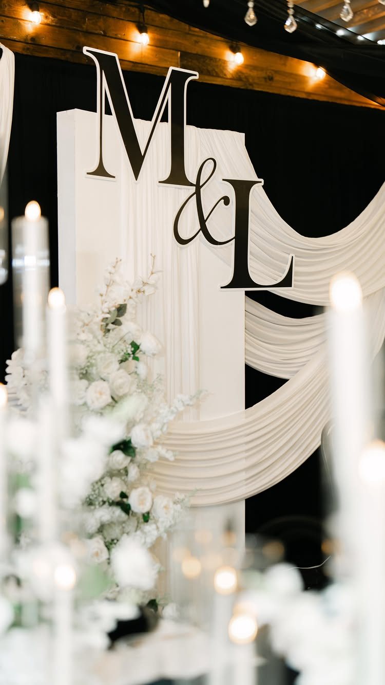 13 Black and White Wedding Decor Ideas for an Elegant Celebration 4 Large black initials M and L on a white draped backdrop with white flowers.