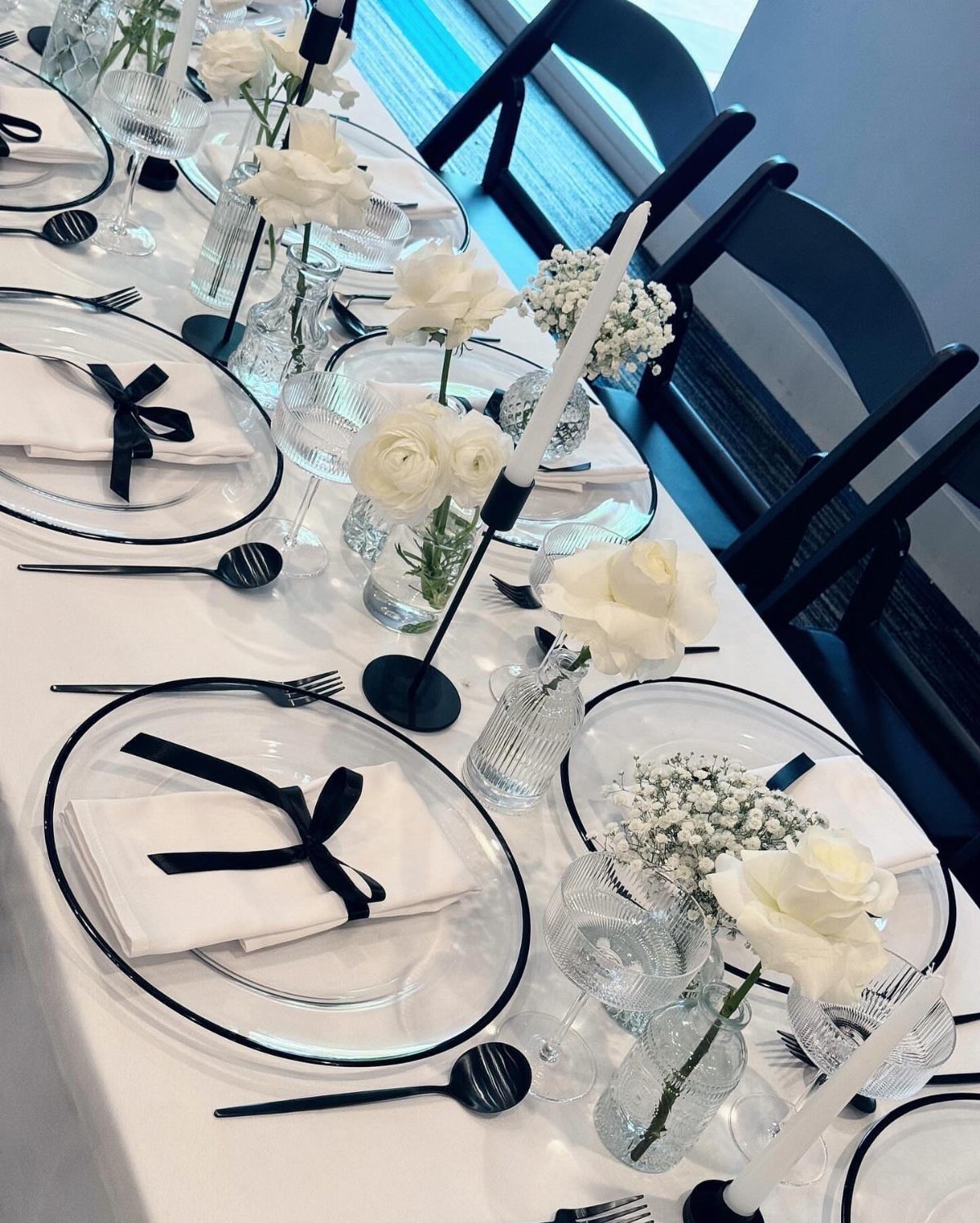 13 Black and White Wedding Decor Ideas for an Elegant Celebration 9 A wedding table set with white tablecloths, black-rimmed plates, white roses, and black ribbons.