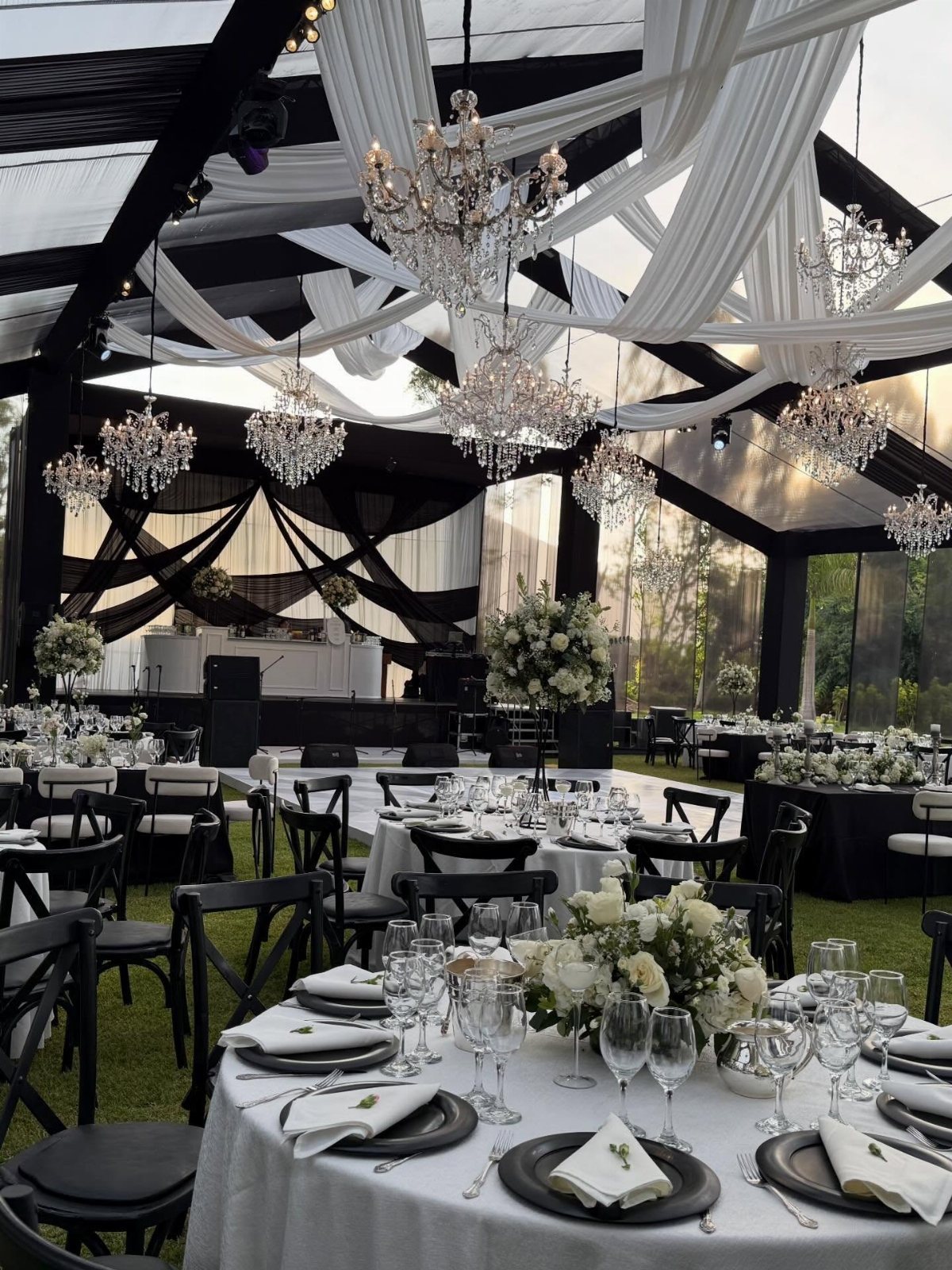 13 Black and White Wedding Decor Ideas for an Elegant Celebration 12 Wedding tables with white linens, black plates, and white floral centerpieces under a draped tent.
