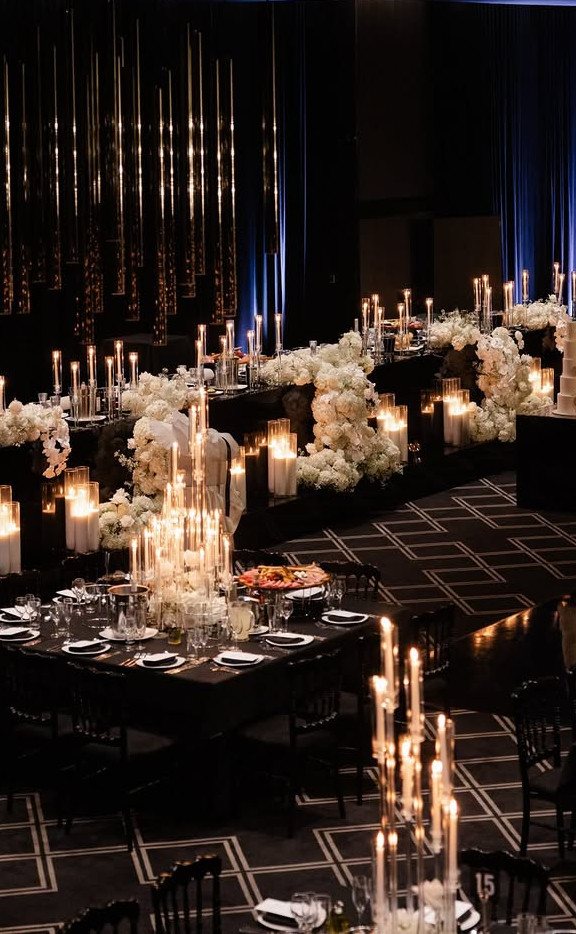 13 Black and White Wedding Decor Ideas for an Elegant Celebration 3 Elegant wedding tables decorated with white flowers, black linens, and many glowing warm taper candles.