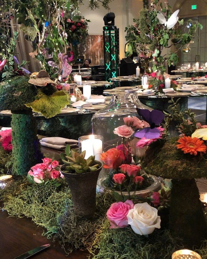 Pink and white roses with lit candles and succulents arranged in green moss on a table.