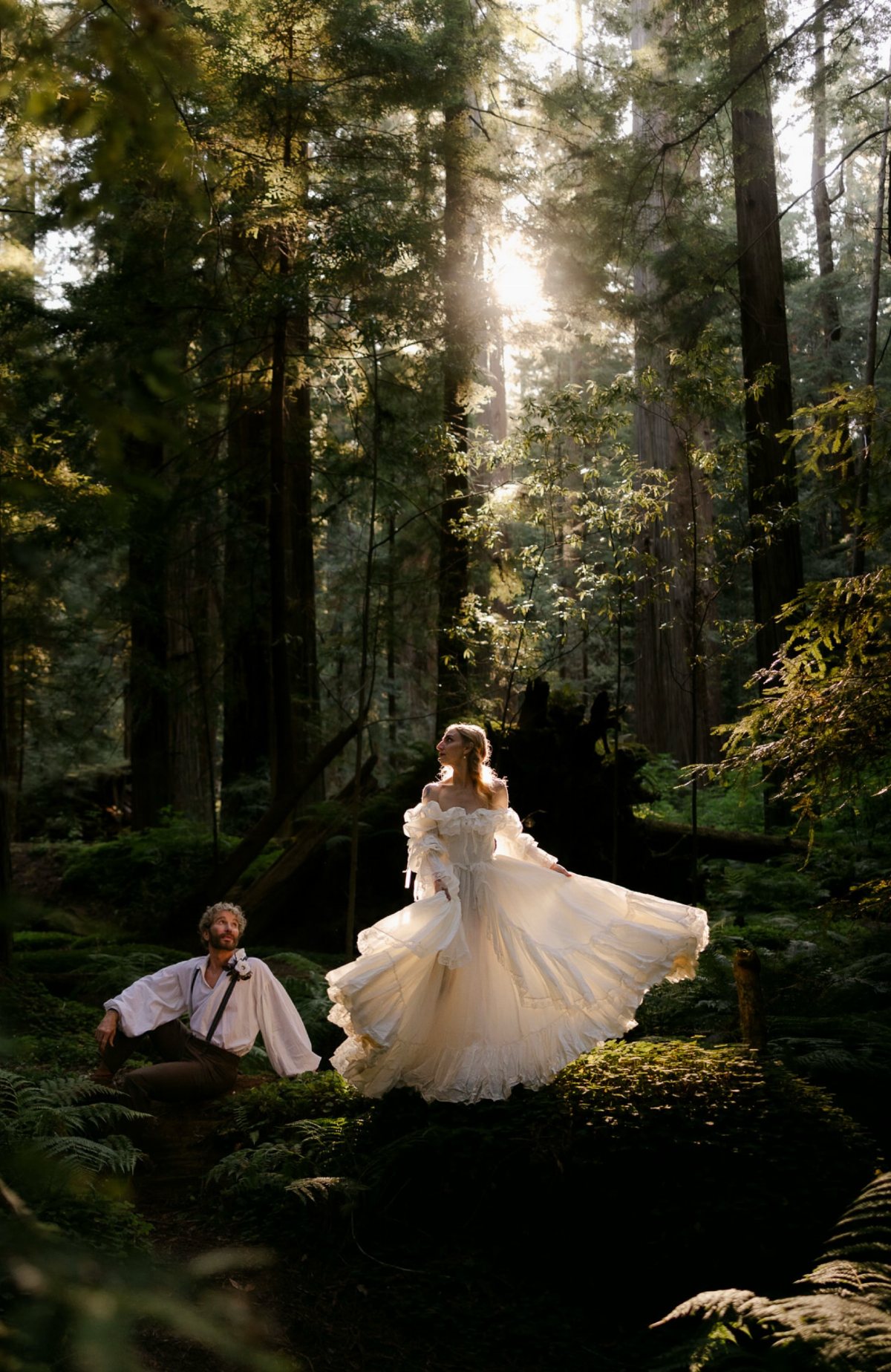 A bride in a white ruffled gown twirls in a sunlit, lush forest setting.
