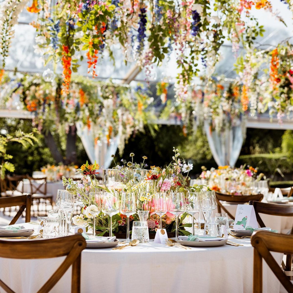 Floral centerpieces and hanging flowers decorate a wedding reception table under a clear marquee tent.