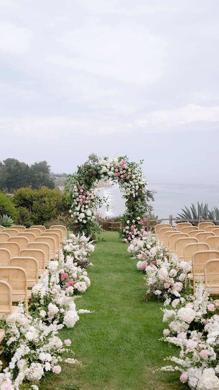 Floral arch with pink and white flowers overlooking the ocean at a wedding ceremony.