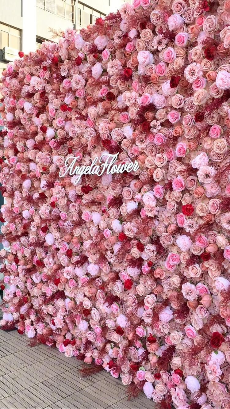 A large wall of pink and red roses with a white sign reading Angela Flower.