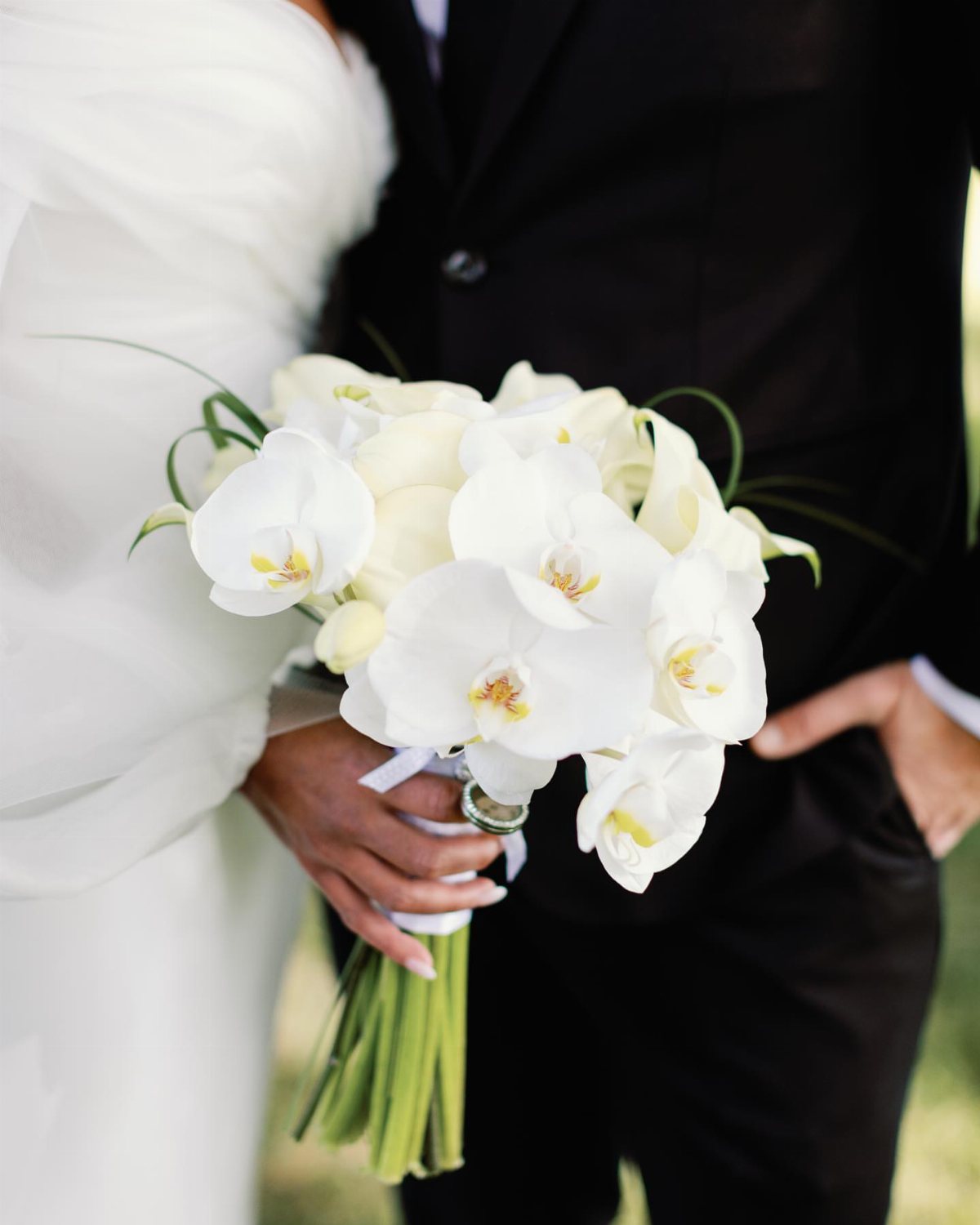 A white orchid bouquet held by a bride and groom during a wedding.