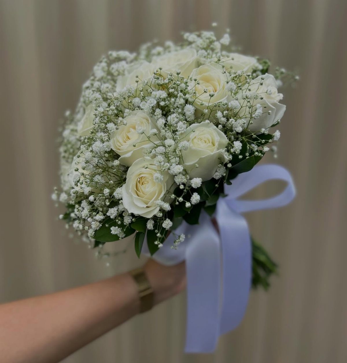 A hand holding a bouquet of white roses and baby's breath tied with a white satin ribbon.