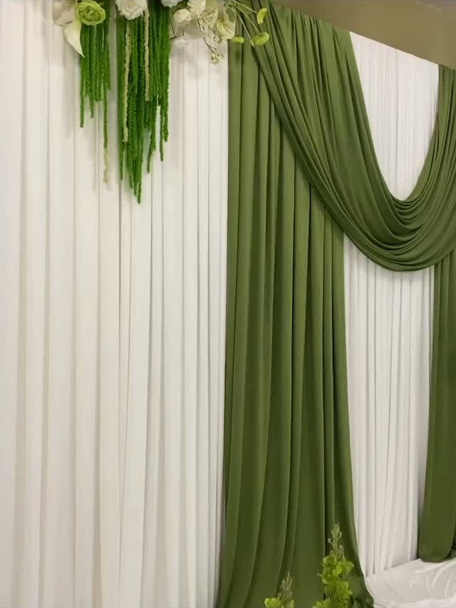 White pleated curtains with draped olive green fabric and hanging green floral decorations.