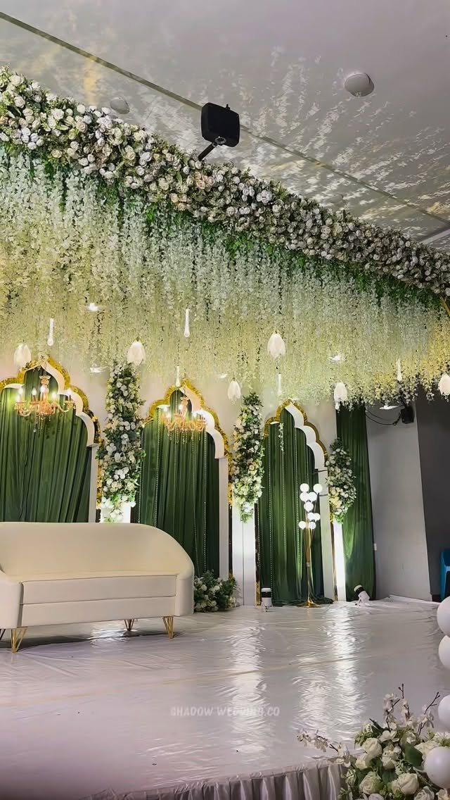A wedding stage featuring a white sofa, green drapes, and hanging white floral decorations.