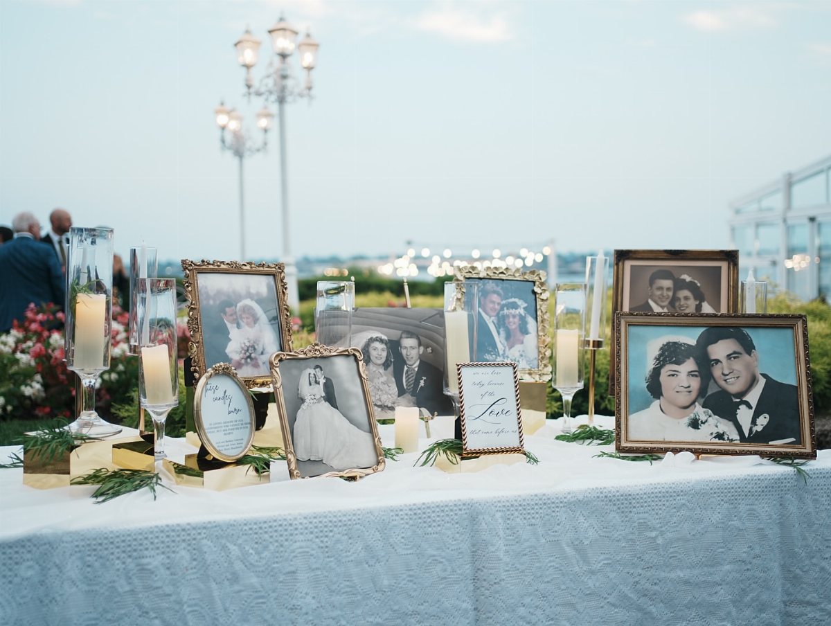Framed vintage wedding photographs and lit candles arranged on a light blue tablecloth outdoors.