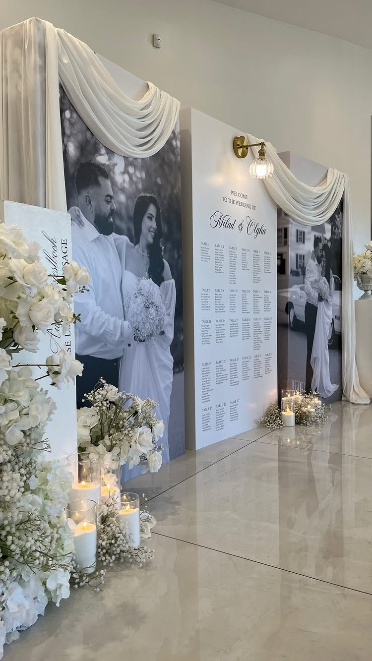 Large black and white wedding portraits displayed on white panels with floral arrangements and candles.