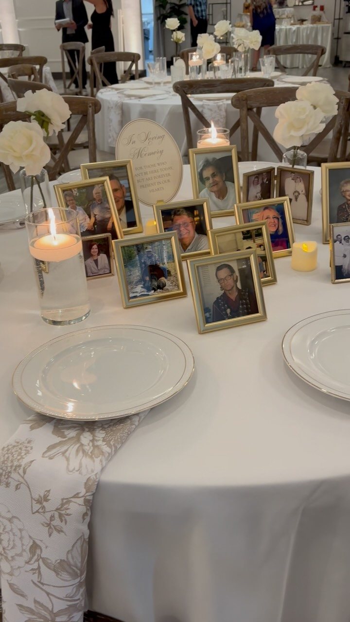 Gold-framed portraits of loved ones arranged on a white wedding table with candles.