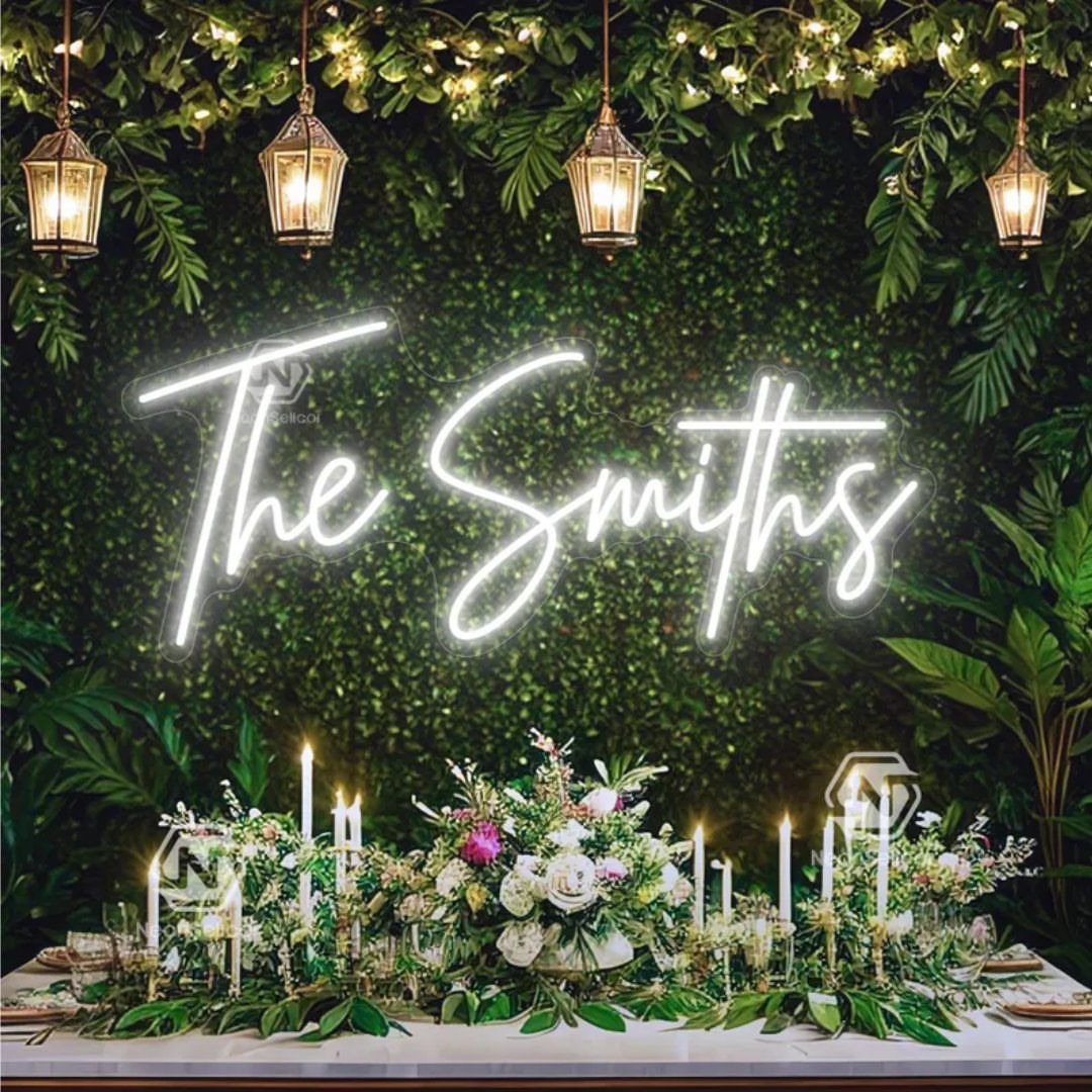 White neon sign reading The Smiths mounted on a green foliage wall above a floral table setting.